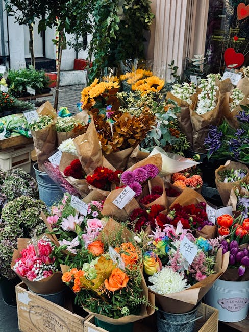 An outdoor display of freshly arranged flower bouquets featuring a variety of blooms including bright yellow sunflowers, deep red and pink roses, white lilies, purple statice, and orange gerbera daisi