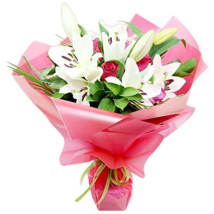 An elegant, professionally arranged bouquet of white lilies and red roses stands upright against a pure white background, the flowers presented as if ready for same-day delivery across Sipson. Dominating the composition are several impressive white Oriental lilies, each with wide, open petals that taper to soft points, creating a star-like silhouette. Their centres hold dark reddish-brown stamens, some dusted with pollen, providing a dramatic contrast against the clean white petals. A few elongated lily buds, still closed and tinged with pale green and cream, peek out from the foliage, promising that the bouquet will continue to change and open, day by day, in the recipient's home. Threaded carefully between the lilies are multiple deep red roses, many in bud and some partially open, their velvety petals tightly layered to form classic, romantic spirals of colour. Around and beneath these blooms, a thick layer of lush greenery creates both structure and softness, combining broad, glossy leaves with slimmer, grass-like strands that arc gracefully upwards, much like the wind-ruffled plants that border the roads around Sipson and the nearby Bath Road. Wrap-around bright pink cellophane or floral paper flares outwards from the base in generous, translucent folds, its gleaming surface catching highlights that lend a sense of luxury and festivity. A slim lime green ribbon is tied with care at the stems, forming a small bow and trailing ends that sit neatly against the vivid pink wrap. The overall impression is one of refined celebration and heartfelt emotion, ideal for anniversaries, milestone birthdays, or thoughtful thank-you gestures delivered to homes and offices around Sipson.