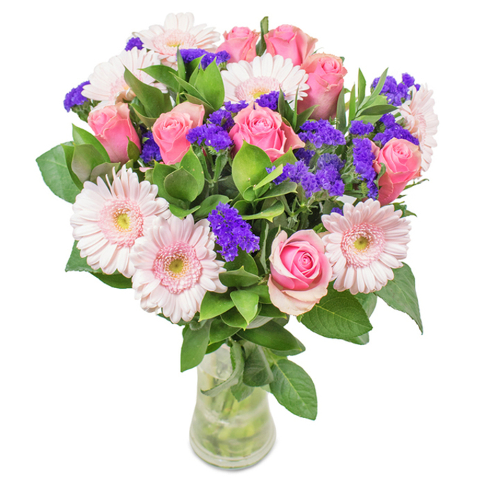 Presented against a minimalist white background, this vibrant bouquet captures the fresh spirit of Sipson in every detail. The arrangement is centered on approximately seven to nine petite, tender pink roses, many just beginning to open and reveal their classic spiral interiors-each one a symbol of new beginnings and cherished affection. Accenting these are five to seven pale pink Gerbera daisies, their generous daisy-like heads and lighter, almost silvery centers lending an aura of soft radiance. Interlaced throughout are sprigs of intense purple statice, their crisp, textured blooms adding a bold pop of colour and contemporary contrast, reminiscent of local wildflowers glimpsed along the Sipson Road verge. The arrangement is encircled by an abundance of dewy, dark green foliage, whose rich tones anchor the bouquet with a hint of woodland freshness-bringing to mind early walks through local parks. All stems are gathered in a simple, transparent glass vase, allowing the natural lines and movement of each flower to shine. Whether gifted to mark a birthday, an anniversary, or as a thoughtful surprise, this bouquet celebrates Sipson's lively community and warm-hearted spirit, making it an ideal floral accent for any moment of joy or heartfelt appreciation.