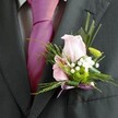 There's a refined charm in this Sipson-inspired boutonniere, depicted in exquisite detail as it adorns the pristine lapel of a dark charcoal jacket. The central rose, a soft blush pink, unfolds its petals with quiet confidence, each curve washed in natural light, as if the gentle sunrise over Sipson's fields has been captured within its bloom. Tucked beside it, a pink alstroemeria painted with bolder fuchsia veins provides both visual interest and a splash of local vibrancy, while a verdant green chrysanthemum acts as a lively focal point. Wispy sprigs of fern and swathes of glossy, narrow foliage act like a green embrace, their textures reminiscent of hedgerows nearby Sipson Village Green. Clusters of ethereal white gypsophila hover around the blooms, lending a touch of innocence and tradition. Completing the design is a slender, shimmery lavender ribbon - neatly tied and thoughtfully chosen to mirror the festive tie beneath - ensuring everything harmonises for the special day. Worn for a wedding, prom, or another celebration, the piece radiates not just style and floral artistry, but a sense of local pride and fresh beginnings, as perfectly suited to a joyful event in Sipson as to any heartfelt gathering.