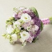 A lush and joyful bouquet, expertly composed to reflect the quiet sophistication and community spirit of Sipson. Large, multi-layered white Lisianthus take centre stage, their softly ruffled petals catching the rich, diffuse daylight and hinting at gentle floral fragrances. Accompanying them are delicately clustered lavender and blush pink stock flowers, creating a tapestry of pastel tones and airy texture-reminiscent of blossoms blooming along Little Harlington fields in early summer. Unexpected splashes of deep purple from Allium 'Star of Persia' orbs emerge between the gentler hues, giving the bouquet a sense of modern flair and artistic surprise. Slender, bright green foliage loops and twists through the arrangement, while the occasional unopened Lisianthus bud adds freshness and promise. The entire bouquet forms a pleasing, rounded shape with just a hint of elongation-a classic hand-tied style beloved in local Sipson celebrations. At the base, a vivid fuchsia pink satin ribbon is wrapped meticulously around the stems and crowned with a spiral of white pearls, lending a sense of refined occasion. The bouquet rests upon a subtly textured, neutral-toned surface that allows each colour and form to stand out, suggesting that this is much more than a simple arrangement-it is a heartfelt expression, suitable for a bride heading to a ceremony at Sipson Community Centre or as inspiration for a romantic dinner at home. Freshness, artistry, and a sense of joyful possibility bloom from every petal.